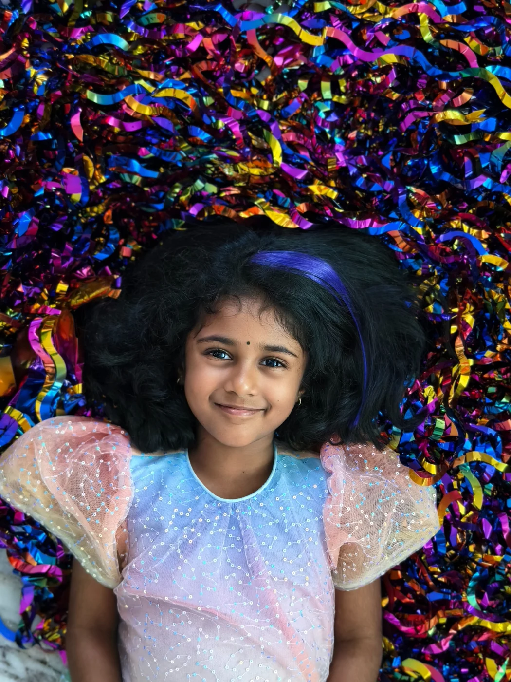 Siya smiling in a sparkly pastel dress with colourful confetti around her