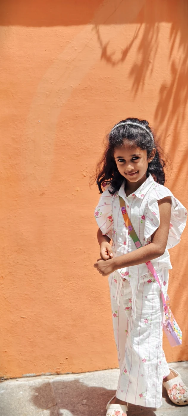 Siya smiling in a white floral outfit against an orange wall